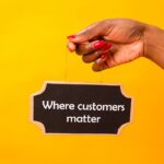 Hand holding a sign with 'Where customers matter' on a vibrant yellow backdrop.